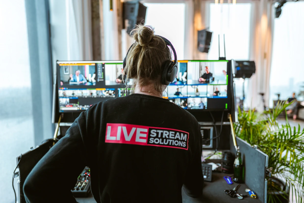 Crewlid van Livestream Solutions bedient de regie van een livestream op locatie, met multiview-monitoren waarop de sprekers en de online deelnemers te zien zijn.