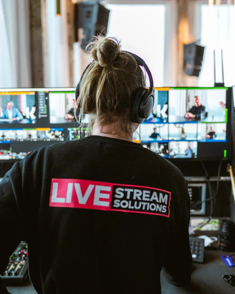 Crewlid van Livestream Solutions met koptelefoon achter de regie, met de deelnemers op de multiviewmonitoren.